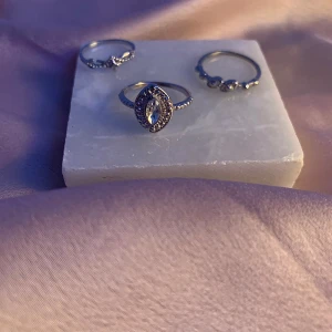 Set med tre silverringar - Säljer ett set med tre eleganta silverringar. En av ringarna har en vacker marquiseformad sten i mitten, omgiven av små gnistrande stenar. De andra två ringarna har enkla men stilrena detaljer. Dom tappar dock färg efter ett tag (3 veckor typ) vid kontakt av vatten.