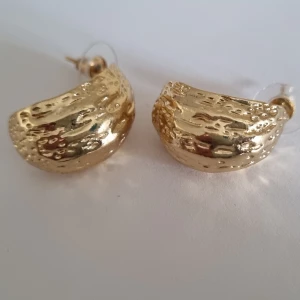 Örhängen 18k guldplätering  - Örhängen med struktur Rostfritt stål + 18k guldplätering   Oanvänt enbart uttagen ur förpackning för fotografering.  