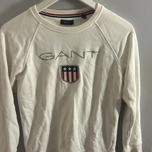 Vit långärmad tröja från GANT - Säljer en stilren vit långärmad tröja från GANT med broderad logga och emblem på bröstet. strl är 146/152 vilket jag skulle säga passar xxs eller xs. Skön och mjuk i materialet!