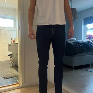 Mörkblå jeansbyxor - Säljer ett par mörkblå jeansbyxor i slim fit. De har en klassisk design med dragkedja och knapp framtill. Perfekta för både vardag och fest! Passar bra till en avslappnad stil eller kan kläs upp med en snygg skjorta.