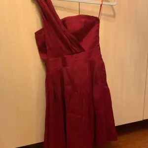 Snygg vinröd oneshoulder klänning perfekt för festliga tillfällen. Den har en elegant design med en axel och en fin passform som framhäver figuren. Materialet ser ut att vara av satin vilket ger en lyxig känsla. Perfekt för en kväll ute eller en speciell händelse.