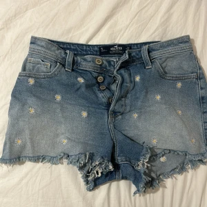 Jeansshorts med blommor från Hollister - Säljer ett par snygga jeansshorts från Hollister med söta små blommor broderade över hela tyget. Midwaist i storlek w27