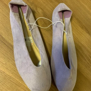 Lila mocka ballerinaskor - Säljer ett par snygga lila ballerinaskor i mjuk mocka. De har en stilren design med rundad tå och en liten klack. Perfekta för både vardag och fest! Skorna är i nytt skick och kommer i storlek 40.