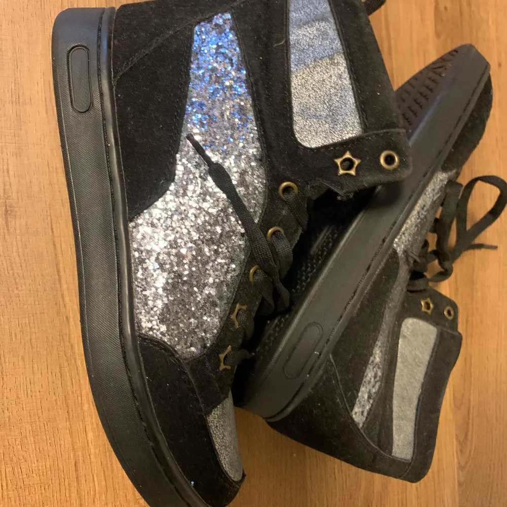 Säljer ett par coola svarta höga sneakers med glittriga silverdetaljer. Skorna har snörning och små stjärnor vid snörhålen som ger en unik touch. Perfekta för att lysa upp vilken outfit som helst! 🖤✨använd 1-2 gånger max. Skor.