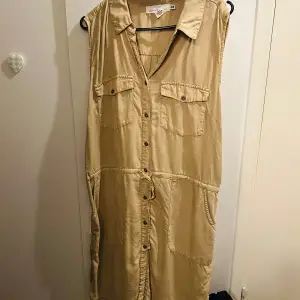 Säljer en beige ärmlös klänning från H&M i storlek XL. Klänningen har knappar framtill och två bröstfickor. Perfekt för en avslappnad sommarlook. Den är i mycket bra skick och har en bekväm passform.