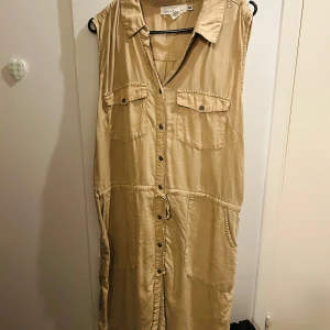 Beige ärmlös klänning från H&M - Säljer en beige ärmlös klänning från H&M i storlek XL. Klänningen har knappar framtill och två bröstfickor. Perfekt för en avslappnad sommarlook. Den är i mycket bra skick och har en bekväm passform.
