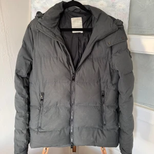 Grå pufferjacka från J.Lindeberg - Säljer en snygg grå pufferjacka från J.Lindeberg. Den är perfekt för kalla dagar med sin tjocka vaddering och har en praktisk huva. Jackan har dragkedja framtill och två fickor med dragkedjor. Märkesloggan sitter på ärmen. Perfekt för vintern!❄️Notera sista bilden att ögglan är lös.