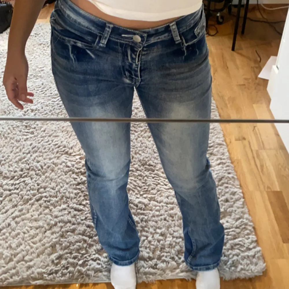 Säljer ett par snygga blå jeans i mycket bra skick. De har en normal passform och är lågmidjade. På bakfickorna finns coola broderade vingar som ger en unik touch. Perfekta för både vardag och fest!. Farkut & Housut.