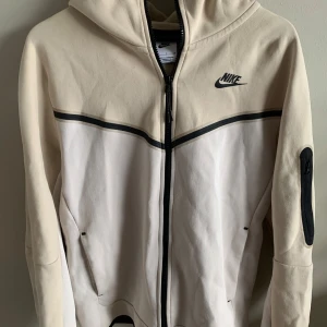 Nike Tech Fleece  - Säljer en snygg beige och vit nike tech fleece i bra skick. Den har en liten fläck som inte går bort där bak (se bild 3) annars inga skador. Skriv för fler bilder eller andra frågor!