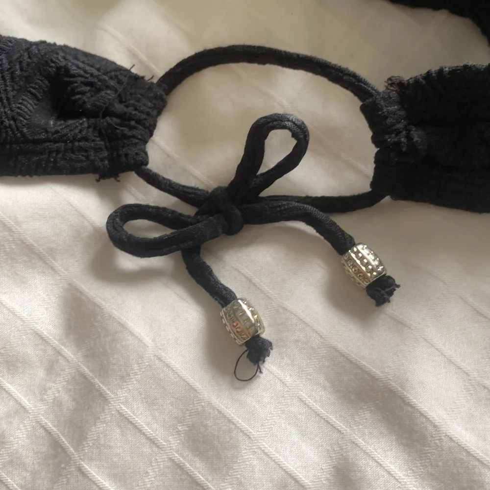 Säljer en superfin svart bikini med spetdetaljer. Överdelen har en klassisk trekantsform med knytband i nacken och ryggen, vilket ger en justerbar passform. Underdelen har också knytband på sidorna för en perfekt passform. Materialet är mjukt och bek. Muu.