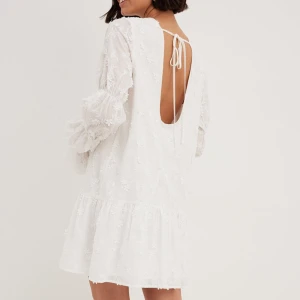 Vit klänning med öppen rygg från NA-KD - Säljer en superfin vit klänning från NA-KD. Den har en öppen rygg med knytband och långa ärmar med volangdetaljer. Storlek 36 och aldrig använd, därav prislapp kvar. Nypris 799kr.