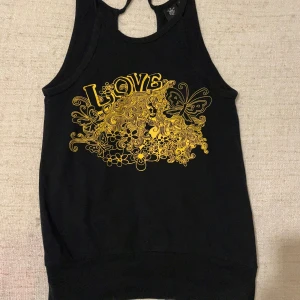 Svart linne från Eve of Eden - Säljer ett svart linne från Eve of Eden i storlek S. Det har ett coolt gult tryck med texten 'LOVE' och en massa blommor och en fjäril. . Linnet är ärmlöst och har en bekväm passform..på bild är jag som mamma men på er unga tjejer är den perfekt på 😊