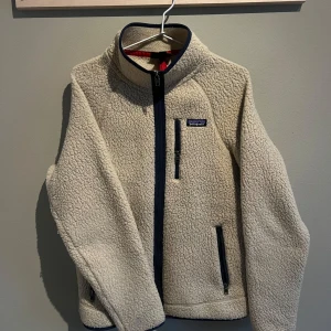 Patagonia Fleece - Säljer min patagonia fleecejacka i färgen khaki.  Den är sparsamt använd och i gott skick, det enda som sticker ut är att den är lite nopprig men går enkelt att ta bort.  Har även klippt bort de röda tyglapparna på dragkedjorna. Nypris ~1700kr.