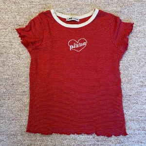 Röd T-shirt med vita ränder, tryck. - Säljer en röd T-shirt i storlek xxs. Pris kan diskuteras. Köpt för länge sen men nästan aldrig använd, bra skick!