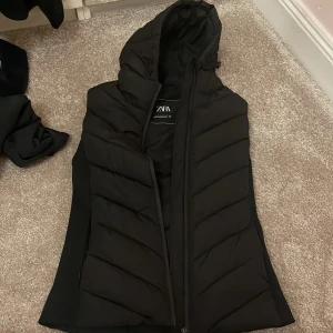 Svart pufferjacka från Zara - Säljer en svart pufferjacka från Zara i storlek XS. Jackan har en dragkedja och är perfekt för höst och vinter. Den är i nyskick och har en snygg, quiltad design med huva. Superbekväm och stilren för kalla dagar!
