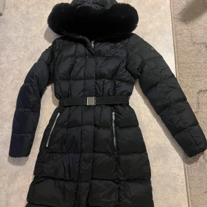 Svart vinterjacka ny - En jätte fin svart vinterjacka från märket AKHA. Använd en gång så i nyskick! Jätte fin och skön. Med bälte i midjan. Storlek 34 men passar 36.