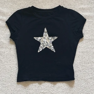 Svart t-shirt med glittrig stjärna från Shein - Säljer en svart t-shirt från Shein i storlek XS. Den har en stor glittrig stjärna på framsidan som verkligen poppar. Lite slitage syns på en söm. Skriv för fler bilder eller frågor!🖤🩶
