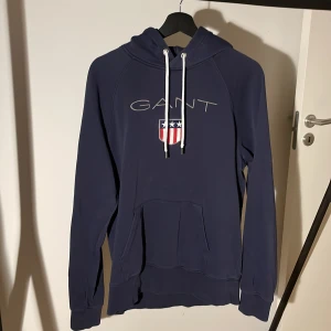 Mörkblå hoodie från GANT - Säljer en snygg mörkblå hoodie från GANT i storlek L. Hoodien är i bra skick och ser fabriksnytt! Nypris: 800kr