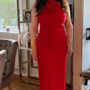 Röd Maxiklänning - Säljer denna vackra röda maxiklänning i storlek 38-40. Den har en elegant blomdetalj vid halsen och är perfekt för festliga eller mer formella tillfällen. Klänningen är i mycket bra skick och har endast använts ett fåtal gånger. Nypris över 1800 kr, 