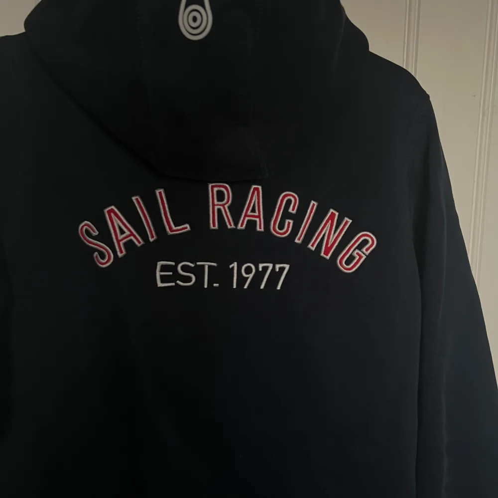 Sail Racing hoodie, nästintill oanvänd. Marinblå färg med text på ryggen.. Hoodies.