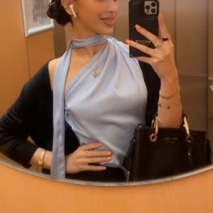 Ljusblå satin oneshoulder topp - Säljer en superfin ljusblå satin topp med oneshoulder-design i storlek S. Den har en elegant knytning vid halsen som ger en extra touch. Perfekt för en utekväll. Toppen är i ett glansigt material.