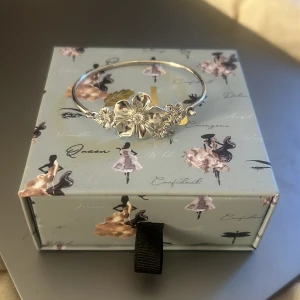 Silver armband från ioaku  - Elegant silverfärgat armband från Jocku by Janny med ett vackert blommotiv i mitten. Perfekt för att ge en stilfull touch till din outfit.