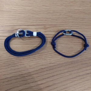 Två blå armband med metallspännen - Säljer två stilrena blå armband med metallspännen. Det ena armbandet har en vit detalj och ett robust spänne, medan det andra har en enkel knutdesign med ett mindre spänne. Perfekta för en avslappnad look. Navy blå grisch.