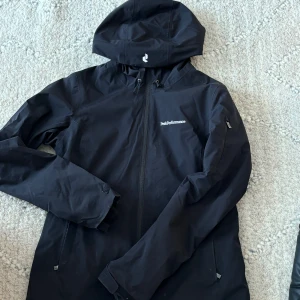 Svart skidjacka från Peak Performance - Säljer en svart skid jacka från Peak Performance med huva och dragkedja. Jackan är figursydd och sitter som en smäck. Den är långärmad och har en insida som ger extra värme. Går att använda både i backen och till vardags. 