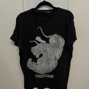 Svart t-shirt med tigertryck från Roberto Cavalli - Snygg svart t-shirt från Roberto Cavalli med ett tigertryck i grått på framsidan. Storleken är S