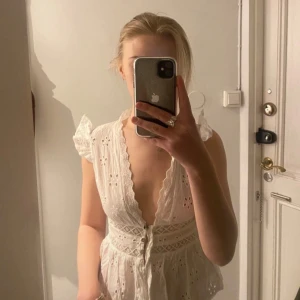 Vit blus med spetsdetaljer - En söt vit blus med vackra spetsdetaljer och broderade blommor. Blusen har en v-ringad design och korta ärmar med volang. Perfekt för en somrig look!