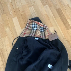 Svart jacka från Burberry - Snygg svart jacka från Burberry med klassiskt rutigt foder. Jackan har en dragkedja och är långärmad. Perfekt för att ge en stilren look.