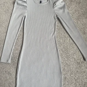 Grå ribbad klänning från Divided - Snygg grå ribbad klänning från Divided med långa ärmar och puffiga axlar. Perfekt för en stilren look. Klänningen har en figurnära passform. 