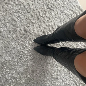 Svarta stövlar med spetsig tå - Snygga svarta stövlar i skinn med spetsig tå och klack. De har en elegant design med dragkedja på sidan för enkel på- och avtagning. Perfekta för att ge en stilren touch till din outfit.