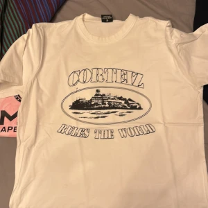 Vit t-shirt med tryck från Cortez - Säljer en vit t-shirt från Cortez med ett stort svart tryck på framsidan som säger 'Cortez Rules The World'. T-shirten har en klassisk rund hals och korta ärmar. Perfekt för en avslappnad stil.