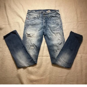 Jack n jones jeans. - Snygga blå jeans från Jack n jones med slitna detaljer och en klassisk femficksdesign. Jeansen har en ljus tvätt och är perfekta för en avslappnad stil. De har en knappgylf och är tillverkade i ett bekvämt denimtyg.