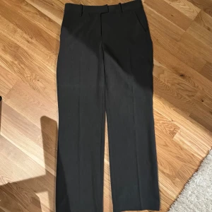 Grå kostymbyxor - Snygga grå kostymbyxor i modellen Maddie, de har medelhög midja och en klassisk rak passform. Byxorna har hällor för bälte och en stilren design. Tillverkade i ett bekvämt material som ger en elegant känsla. De är 81cm ininnerbenslängd. Slutsålda på bikboks hemsida, knappt använda.