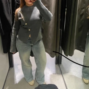 Zara kofta med knappar - Säljer en stilren grå kofta med unika knappar i asymmetrisk design. Koftan har långa ärmar och en elegant passform som passar perfekt för kyligare dagar. Perfekt för dig som vill ha något både bekvämt och snyggt!