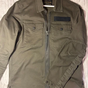 Olivgrön jacka från Replay - Herr jacka från Replay, står ingen storlek för lappen är bortklippt men skulle gissa på S/M. Den är använd men ser nästan ut som ny. Säljer åt min pappa. 