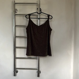 Svart glittrig linnetopp från Jessica - Snygg svart glittrig linnetopp med smala axelband och v-ringning. Perfekt för en kväll ute eller festliga tillfällen. Toppen har en elegant och stilren design som passar till många olika outfits.