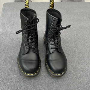 Svarta boots från Dr. Martens - Klassiska svarta boots från Dr. Martens med snörning och den ikoniska gula sömmen runtom sulan. Använda fåtal gånger, nästintill nya. De har en slitning fram på toppen av skon.  #drmartens #vinterskor 
