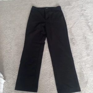 Svarta kostymbyxor från Gina Tricot - Snygga svarta kostymbyxor från Gina Tricot i storlek 36. Byxorna har en klassisk design med raka ben och en diskret dragkedja framtill. Perfekta för en stilren look.
