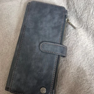 Svart plånbok från CaseMe - Säljer en stilren svart plånbok från CaseMe med plats för kort och mobil. Den har en praktisk dragkedja och ett magnetlås för säker förvaring. Perfekt för att hålla ordning på dina saker med enkel åtkomst. CaseMe Samsung Galaxy S24 Ultra Fodral C30 Series Svart