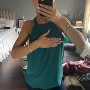 Grön ärmlös topp - sommar25 - Snygg grön ärmlös topp med halterneck-design. Perfekt för varma dagar eller sommarens fester. Toppen har en lös passform och är tillverkad i ett lätt material som ger en bekväm känsla.