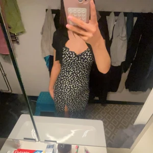 Svart blommig klänning - Säljer en svart klänning med vita blommor. Klänningen har en slits och en v-ringad design som ger en snygg look. Perfekt för sommarens alla tillfällen!