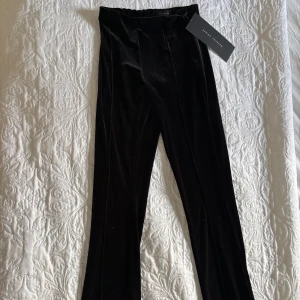 Svarta slits byxor i sammet - Eleganta svarta slits byxor i mjukt sammetstyg. De har en hög midja och en rak passform som ger en stilren look. Perfekta för en kväll ute eller en speciell tillställning.