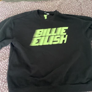 Svart tröja med Billie Eilish-tryck - Säljer en svart tröja med ett coolt grönt Billie Eilish-tryck på framsidan. Perfekt för fans av artisten! Tröjan har en klassisk passform och är gjord i ett mjukt material.