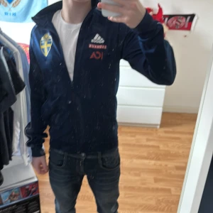 Mörkblå träningsjacka från Adidas - Säljer en mörkblå träningsjacka från Adidas med Sverigelogga på bröstet. Jackan har dragkedja och långa ärmar.