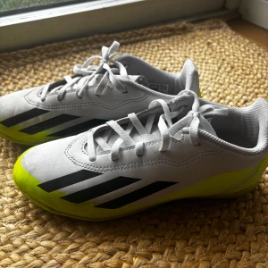 Adidas Crazyfast fotbollsskor - Snygga Adidas Crazyfast fotbollsskor i vitt med svarta och neongula detaljer. Skorna har snörning och en non-marking sula, perfekt för inomhusspel. De har en modern design med tre svarta ränder på sidan och texten 'Crazyfast'. Lite använda, så de är i bra skick.