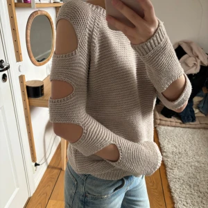 Beige stickad tröja med öppna axlar - Säljer en beige stickad tröja med cut outs. Perfekt för en stilren och trendig look. Tröjan har en bekväm passform och är lätt att matcha med olika outfits. Köpt secondhand och verkar vara handstickad. Står ingen storlek eller märke!