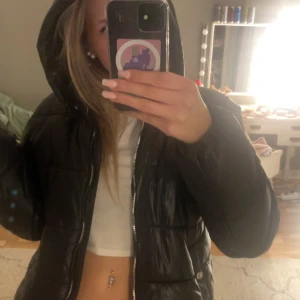 Jacka  - Säljer en svart pufferjacka med huva och dragkedja. Jackan har en glansig yta och är perfekt för kyligare dagar. Den har en normal passform och är långärmad. Perfekt för att hålla värmen med stil! 🖤från only young 